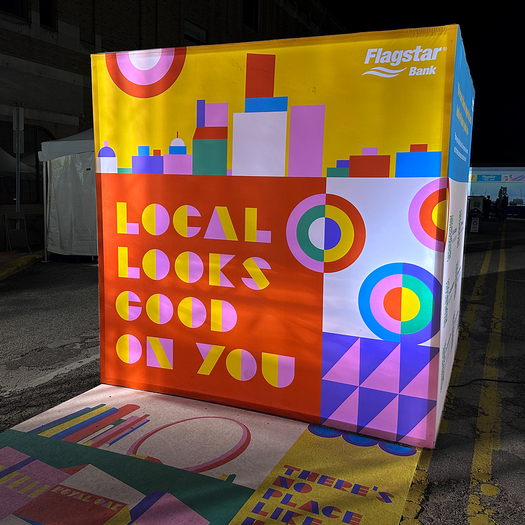 A photograph of a dimensional cube installation at an event with colorful geometric illustration wrapped around it. A photograph of a dimensional cube installation at an event with colorful geometric illustration wrapped around it.